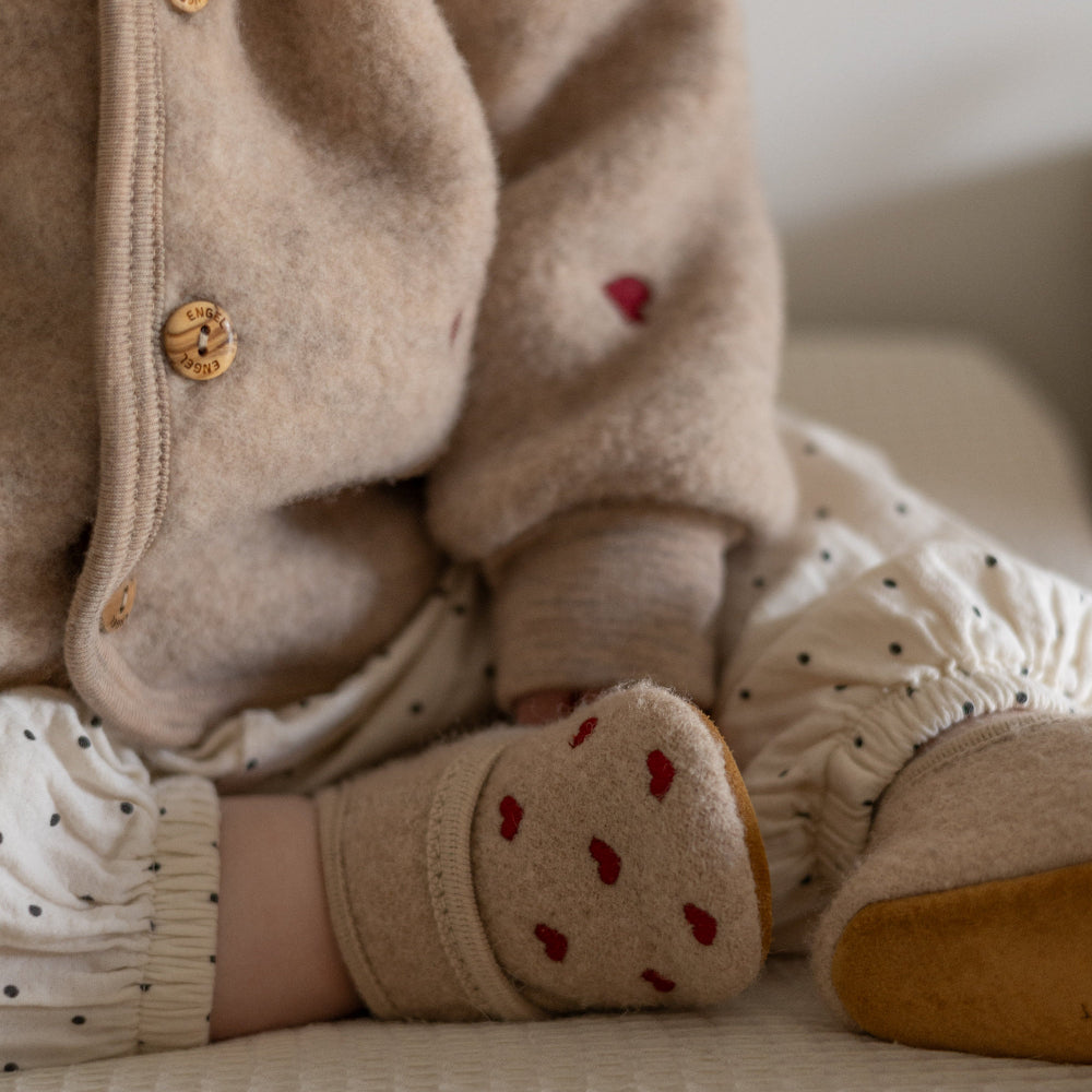 Babyslofjes in beige kleur met hartjes erop aan bij een baby