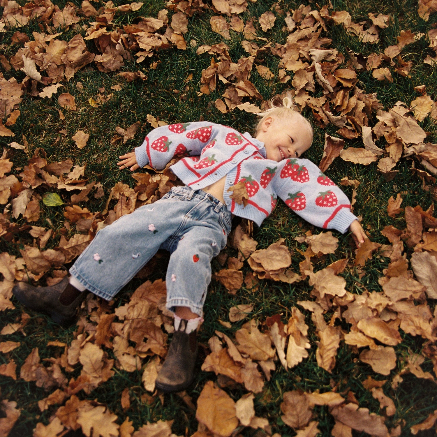Meisjes tussen de bladeren met spijkerbroek van het merk Jujni aan met aardbeien erop