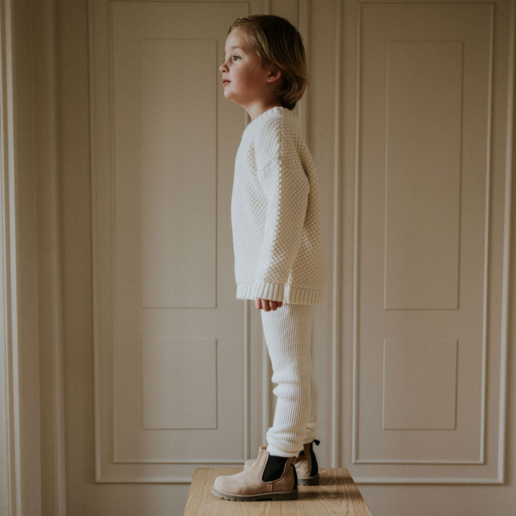 Jongen met wit gebreide trui aan van Yuki en witte legging erbij