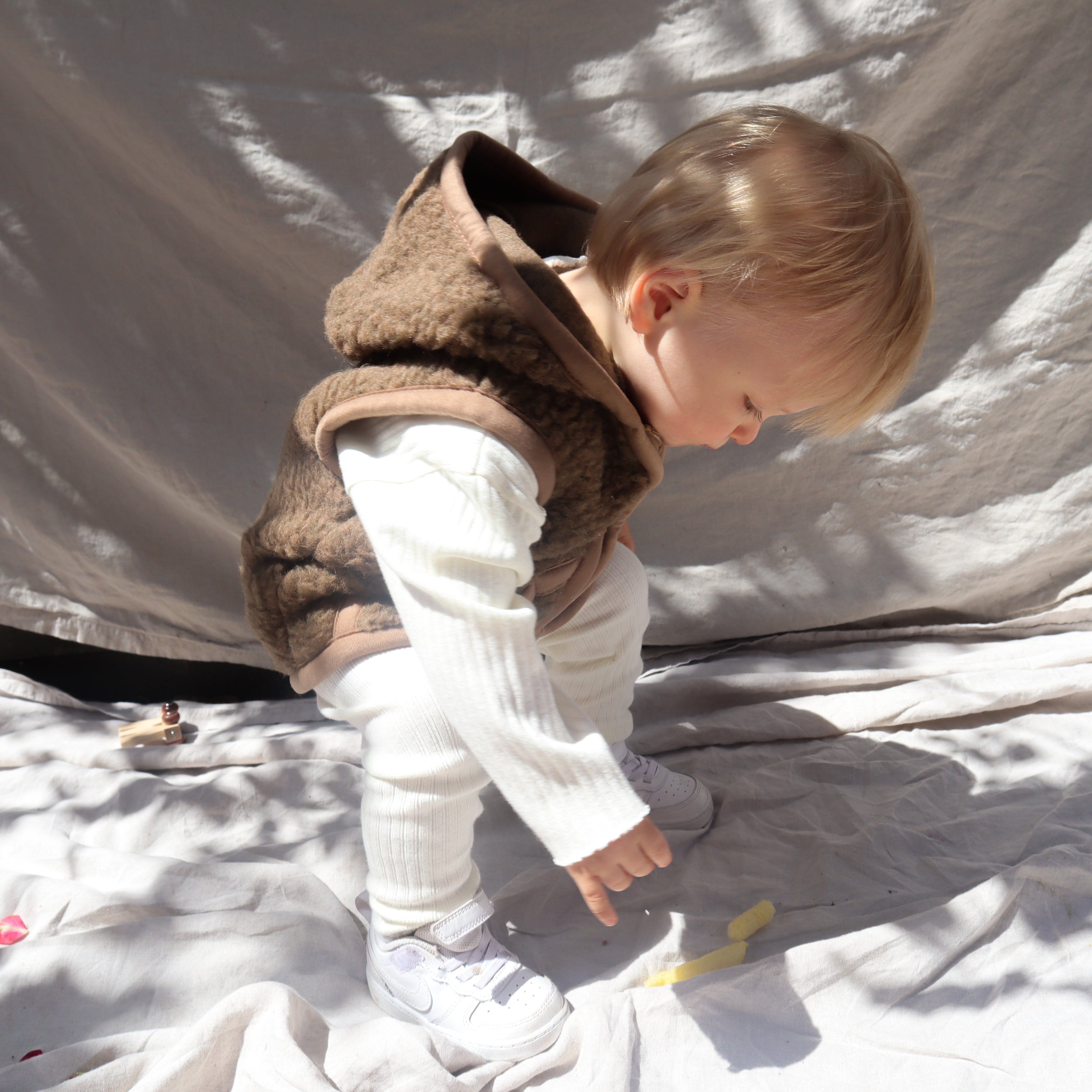 Kind draagt bruine wollen bodywarmer met capuchon van het merk Alwero 