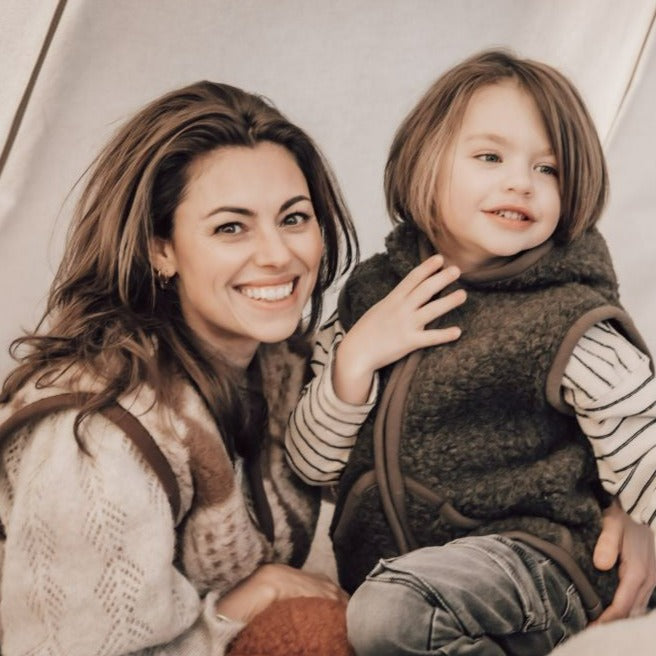 Kind draagt bruine wollen bodywarmer met capuchon van het merk Alwero 